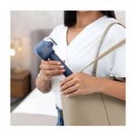 Removedor de pelusas recargable Black+Decker, persona sosteniendo el aparato azul junto a un bolso color beige