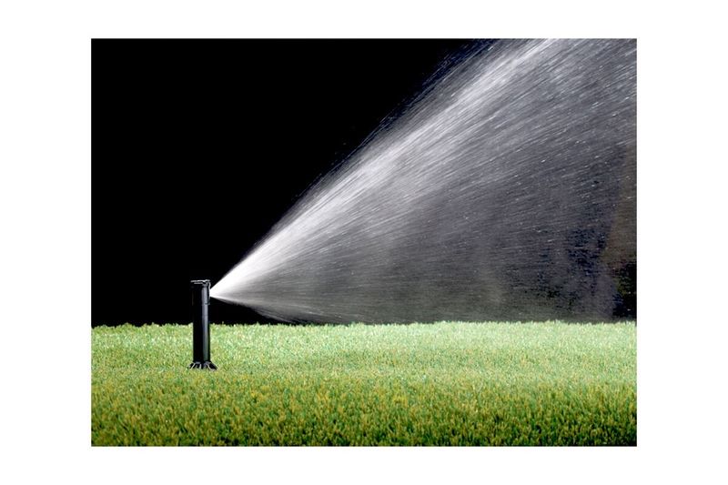 Aspersor para jardín ajustable 1/2 pulgada Rain Bird, funcionando sobre césped verde con chorro de agua en arco