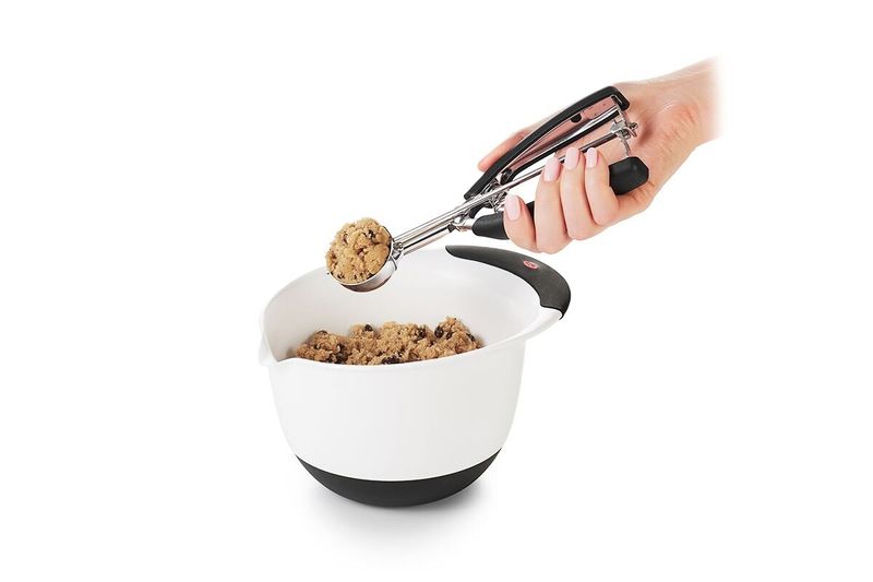 Cuchara para helados y galletas negro acero inox OXO, mano usando el utensilio para sacar masa de un bol blanco