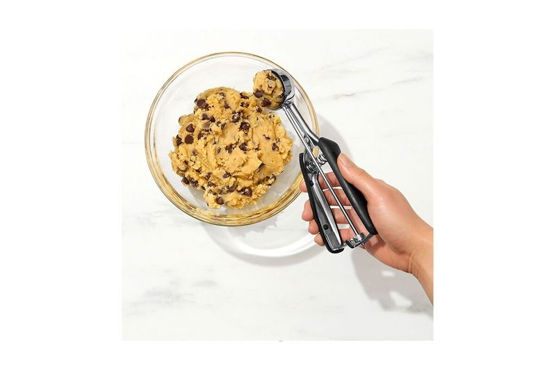 Cuchara para helados y galletas negro acero inox Oxo, siendo utilizada para tomar una porción de masa en un bowl de vidrio