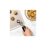 Cuchara para helados y galletas negro acero inox Oxo, mano utilizando el utensilio para servir masa de galletas en bandeja