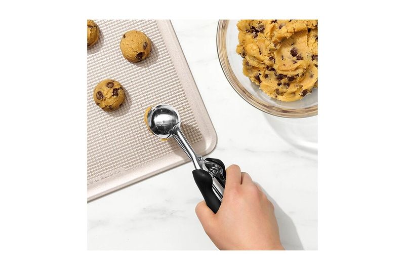 Cuchara para helados y galletas negro acero inox Oxo, mano utilizando el utensilio para servir masa de galletas en bandeja
