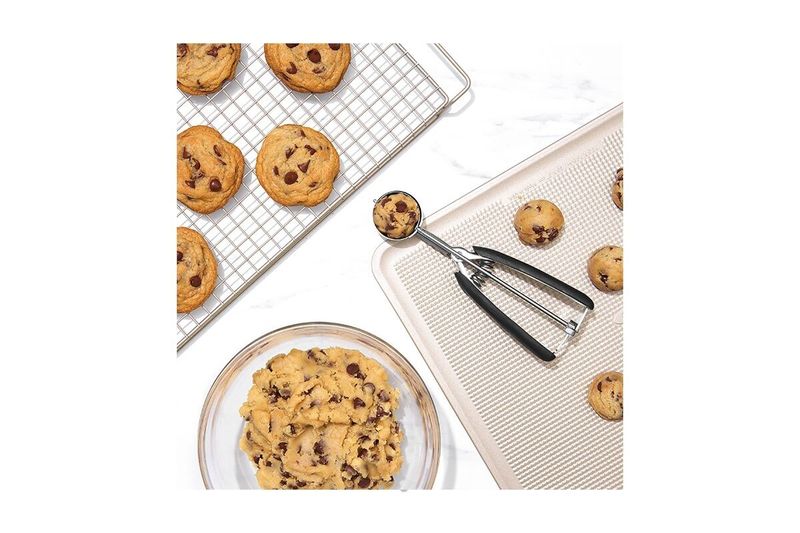 Cuchara para helados y galletas negro acero inox Oxo, en uso sobre bandeja con galletas de chocolate y masa en un bol