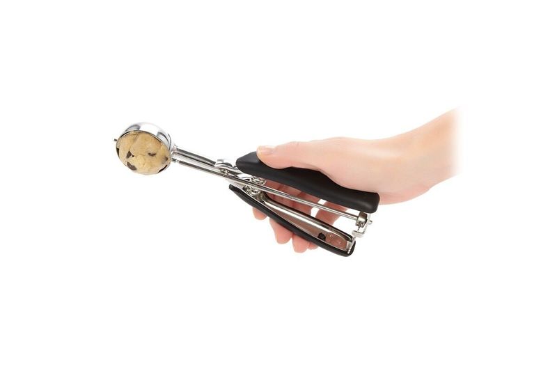 Cuchara para helados y galletas negro acero inox OXO, mano sosteniendo el utensilio con una bola de galleta servida