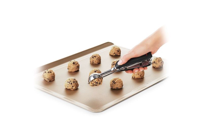 Cuchara para helados y galletas negro acero inox OXO, mano utilizando el utensilio para colocar masa en una bandeja