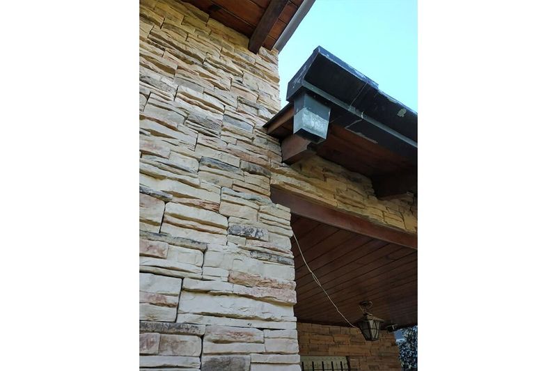 Caja piedra ecológica Kamba arena mate Pirka Stone, instalada en pared exterior con techo de madera y lámpara