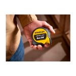 Cinta métrica Control Lock Stanley de 1 pulgada x 8 metros, sostenida por una mano mostrando el frente amarillo y negro