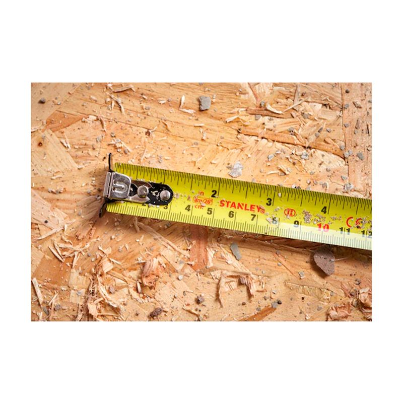 Cinta métrica Control Lock Stanley de 1 pulgada x 8 mts, detalle de la cinta amarilla extendida sobre madera con aserrín