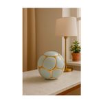 Esfera decorativa 10.5 x 10.5 x 9.5 cm blanco/dorado Concepts, ambientada sobre mesa con lámpara y planta al fondo