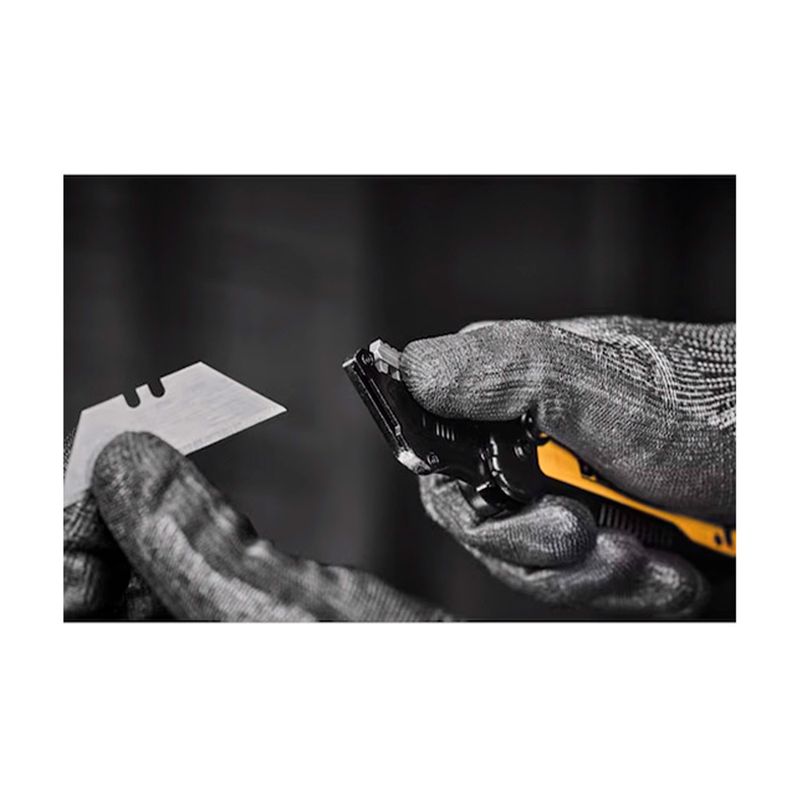 Navaja plegable DeWALT de 31 mm, manos con guantes manipulando la hoja metálica y el cuerpo amarillo de la herramienta
