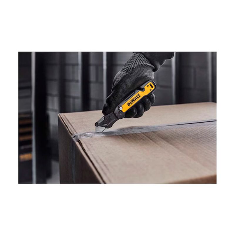Navaja plegable DeWALT de 31 mm, siendo utilizada por una mano con guante para cortar una caja de cartón