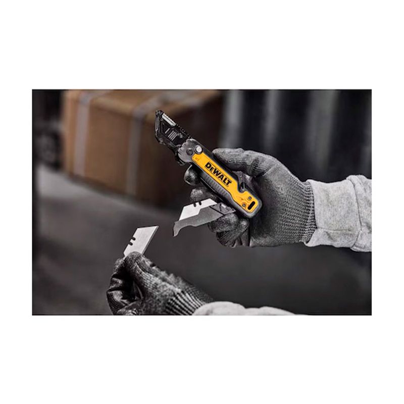 Navaja plegable DeWALT de espacio de almacenamiento 31 mm, sostenida por manos con guantes grises mientras cambian la hoja