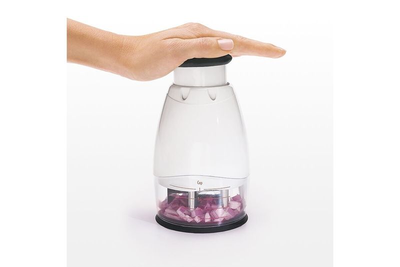 Picador de alimentos pequeño crema Oxo, mano presionando el botón superior con cebollas picadas en el recipiente