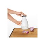 Picador de alimentos pequeño crema Oxo, siendo utilizado por una persona sobre una tabla de madera con trozos de cebolla