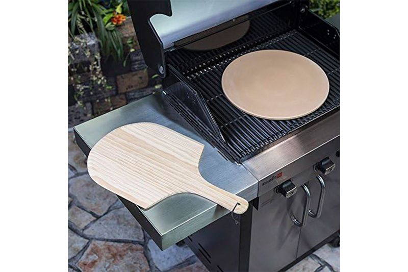 Kit piedra para pizza de 15 pulgadas y paleta madera Char-Broil, colocados sobre una parrilla de acero inoxidable