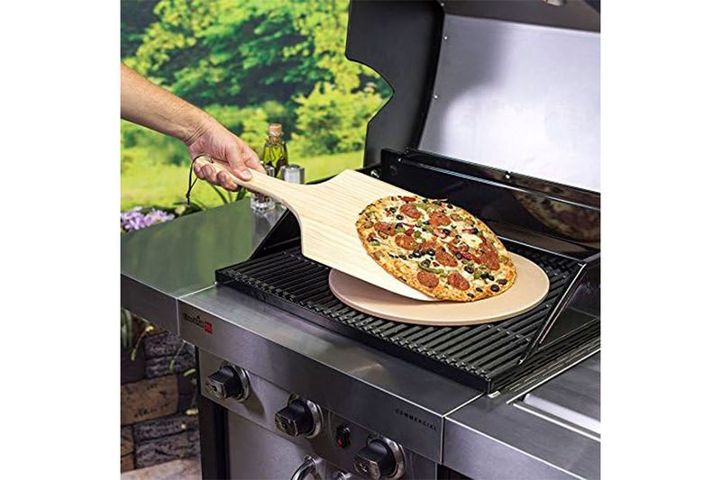 Kit piedra para pizza de 15 pulgadas y paleta madera Char-Broil, paleta deslizando pizza sobre la piedra en una parrilla