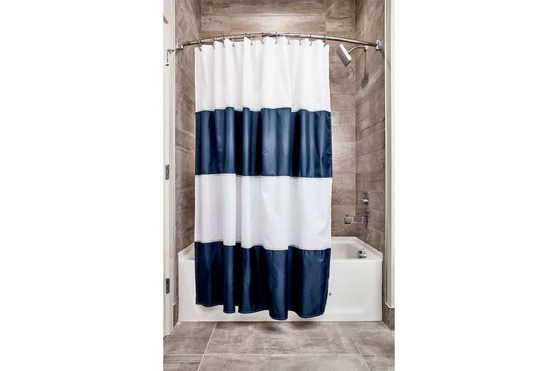 Cortina de baño de tela repelente de agua navy/white Interdesign, instalada en una bañera con franjas azul y blanco