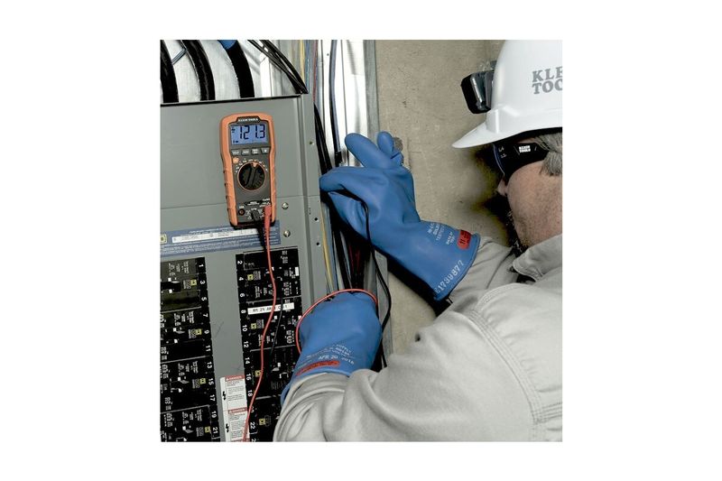 Multímetro digital autorango Klein Tools CAT III, siendo utilizado por un técnico con guantes azules en un tablero eléctrico