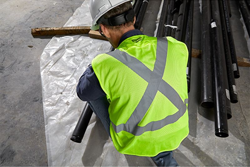 Chaleco de seguridad amarillo 2XL-3XL clase 2 Milwaukee, puesto en un trabajador de espalda junto a tubos negros