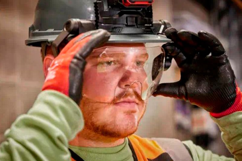 Visor transparente para casco Milwaukee, colocado en la cabeza de un trabajador con guantes ajustando el equipo