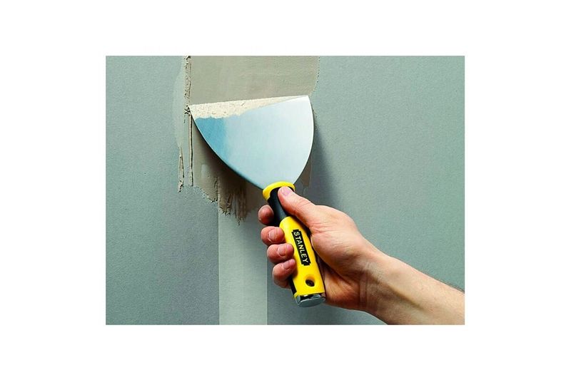 Espátula Stanley de 5 pulgadas para uso en tapicero de acero inoxidable, siendo utilizada para aplicar masilla en una pared