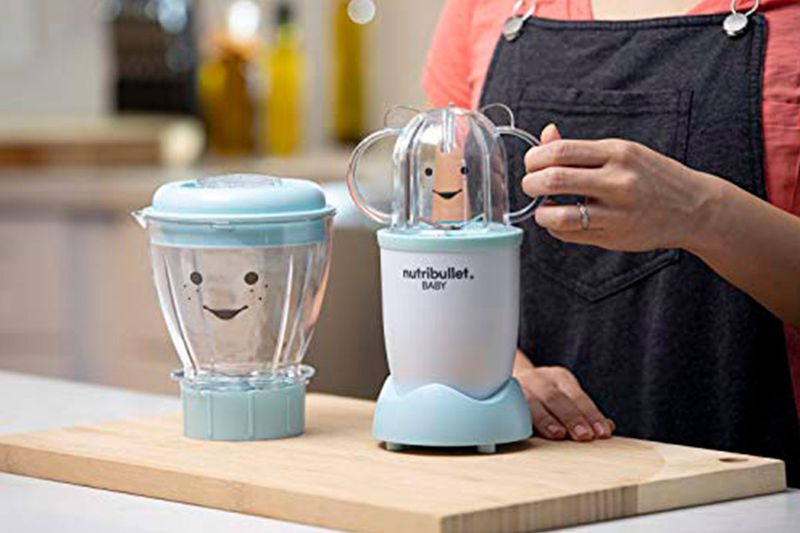 Nutribullet Baby de 18 piezas nutribullet, persona colocando la tapa sobre la licuadora azul en una tabla de madera