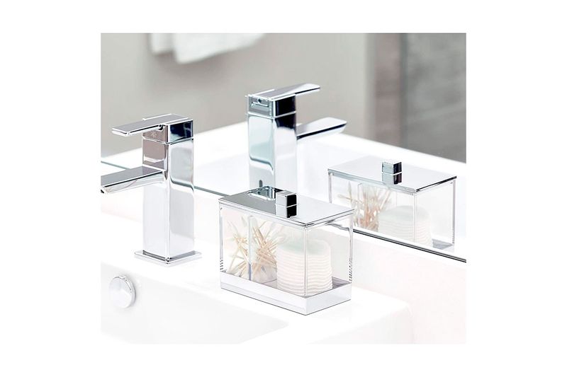 Porta isopos acrílico cromo 5x4 pulgadas iDesign, colocado sobre un lavamanos blanco junto a un grifo cromado