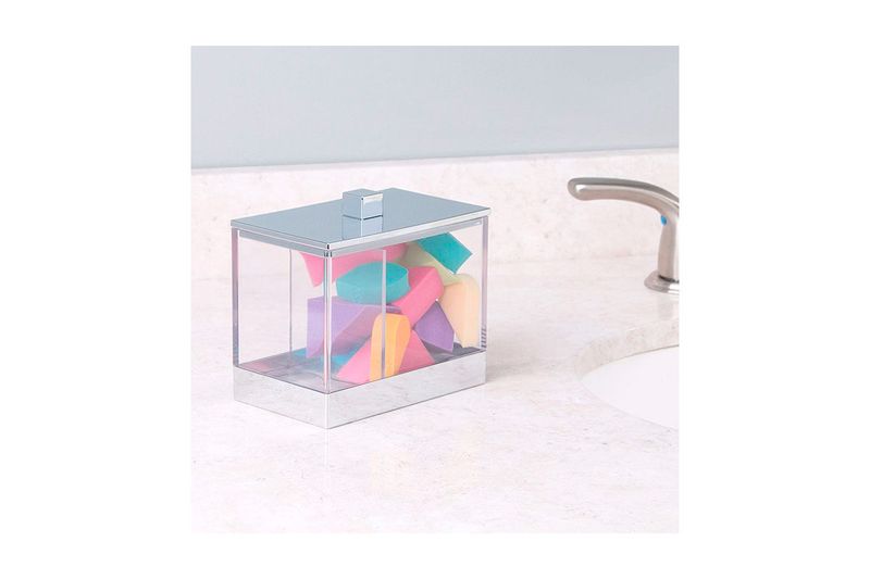 Porta isopos acrílico cromo 5x4 pulgadas iDesign, sobre encimera de baño lleno de isopos de colores y junto al grifo