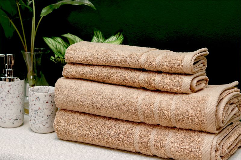 Toalla de baño Nautica de 30 x 60 pulgadas color sand, cuatro toallas dobladas y apiladas junto a accesorios de baño