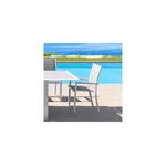 Silla Allure blanco Hespéride, ubicada junto a una mesa blanca en una terraza con piscina y mar al fondo