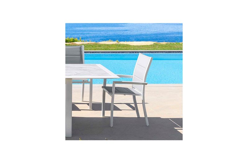 Silla Allure blanco Hespéride, ubicada junto a una mesa blanca en una terraza con piscina y mar al fondo