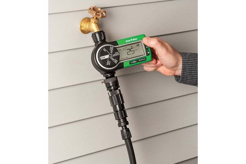 Kit aspersores timer tubos y conectores Rain Bird, mano ajustando el programador digital verde instalado en grifo