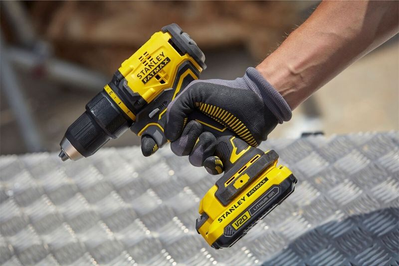 Taladro inalámbrico sin carbón 1/2 pulgada 20V Stanley, sostenido por una mano con guantes sobre superficie metálica