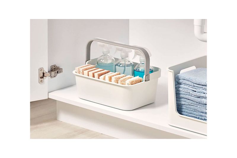 Organizador de almacenamiento con agarre plástico Interdesign, en uso bajo un lavamanos con esponjas y botellas azules