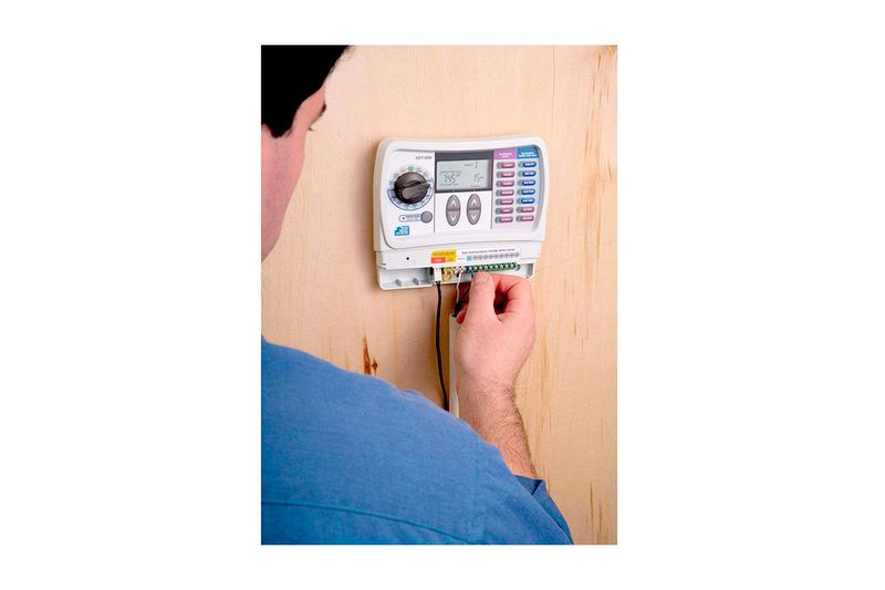 Temporizador de riego 9 zonas Rain Bird, instalado en pared de madera con una persona conectando los cables inferiores