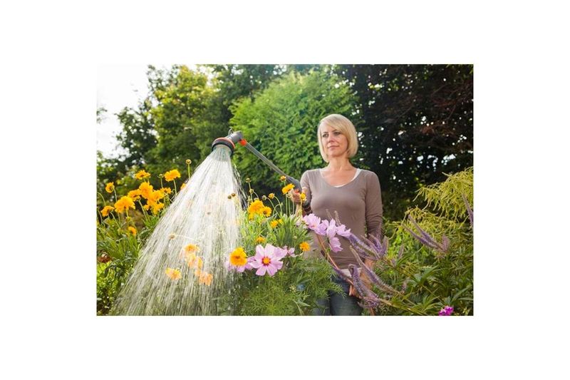 Fusil de riego 2 chorros 90 cm Comfort Gardena, mujer utilizándolo para regar flores amarillas y rosadas en un jardín