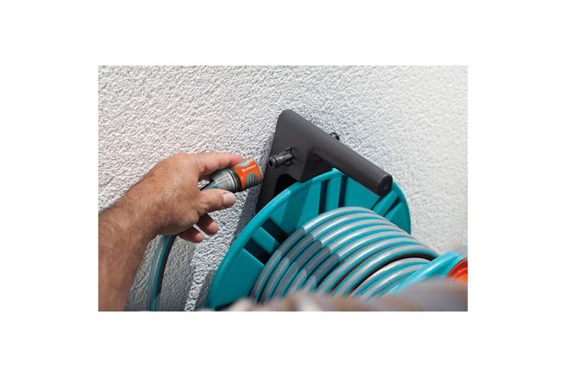 Portamanguera pared 60 m con guía dual fijo/portátil 2650-20 Gardena, detalle de mano colocando manguera en la guía