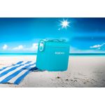 Hielera 11 qt turquesa Tag a Long con correa Igloo, situada sobre arena blanca de playa con una toalla azul al lado