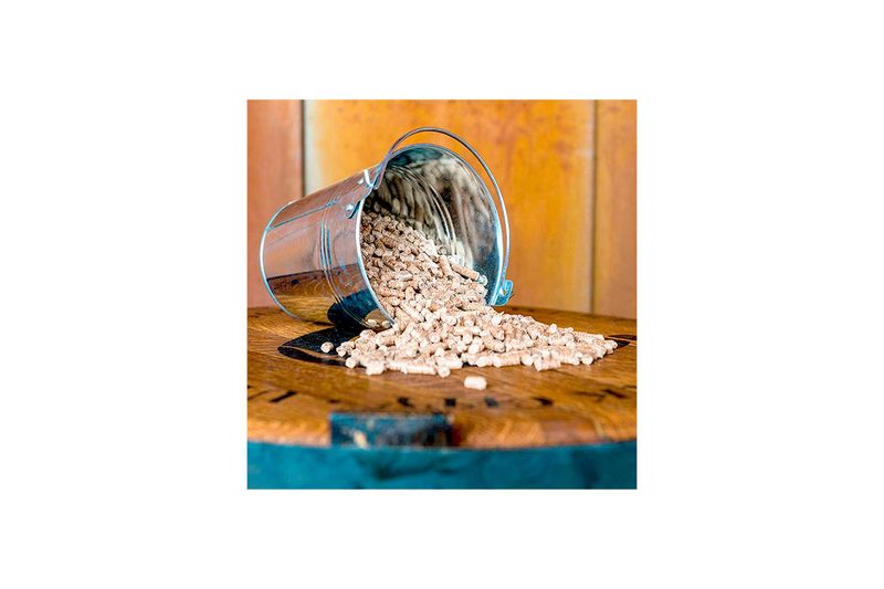 Pellets de madera cherry 20 lb Traeger, vertidos desde un balde metálico sobre una superficie de madera