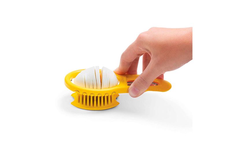 Cortador de silicona amarillo Dreamfarm, mano sosteniendo el mango mientras corta un huevo duro en rodajas