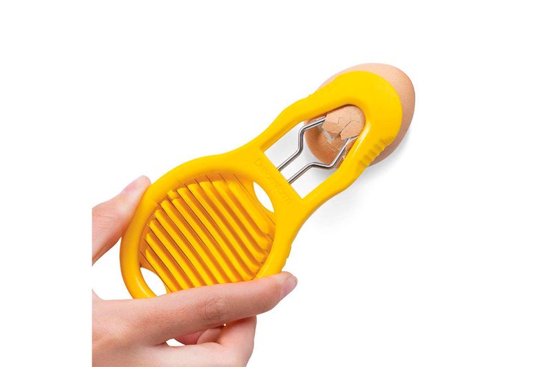 Cortador de silicona amarillo Dreamfarm, mano sujetando el producto mientras rompe la cáscara de un huevo