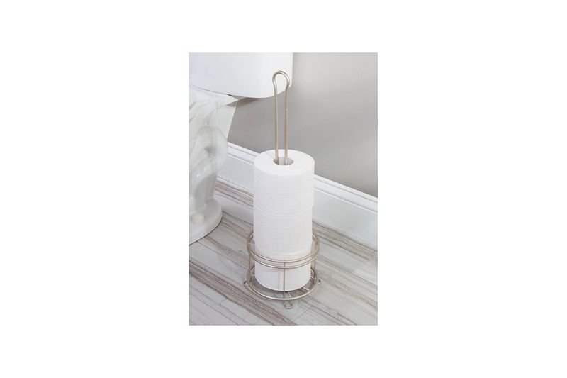 Portarrollo para papel higiénico satín Interdesign, colocado en el suelo junto a un inodoro con tres rollos de papel