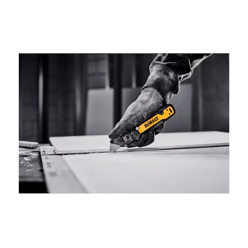 Navaja plegable DeWALT de 31 mm, mano con guante amarillo y negro realizando un corte sobre una superficie blanca