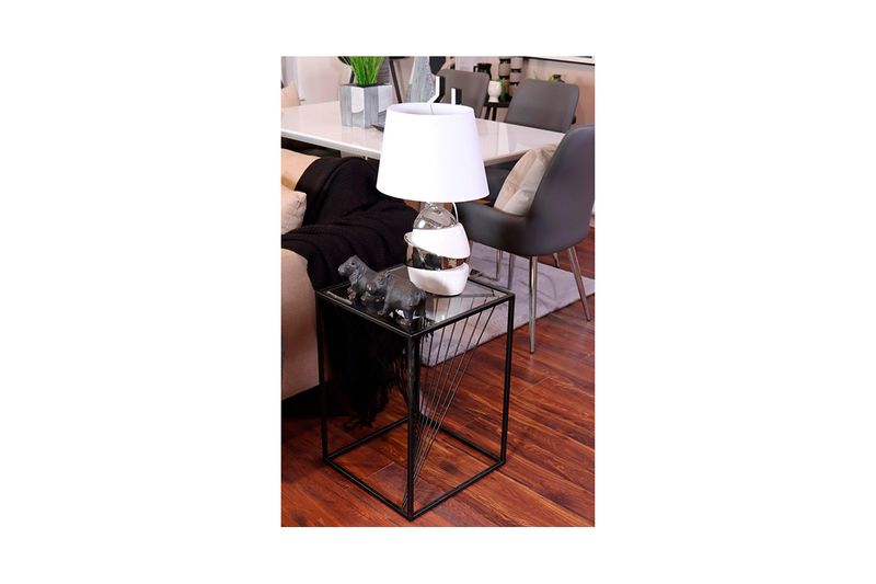 Lámpara de mesa cerámica geométrica blanca/plateada Concepts, encendida sobre mesa auxiliar negra en ambiente decorado