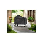 Funda para barbacoa Premium/Deluxe carbón negra Weber, colocada sobre la barbacoa en un patio exterior con plantas