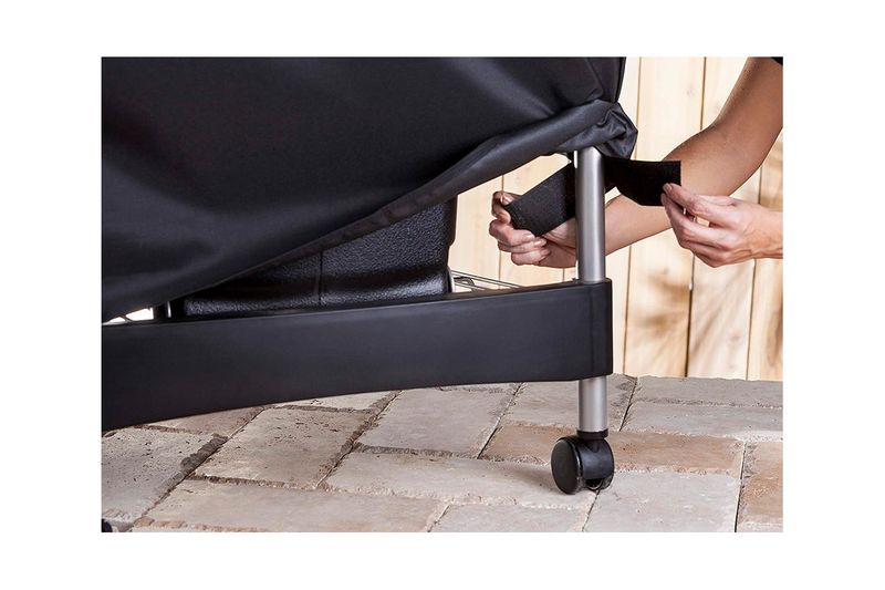 Funda para barbacoa premium/deluxe carbón negra Weber, detalle de manos ajustando la correa en la pata de la barbacoa