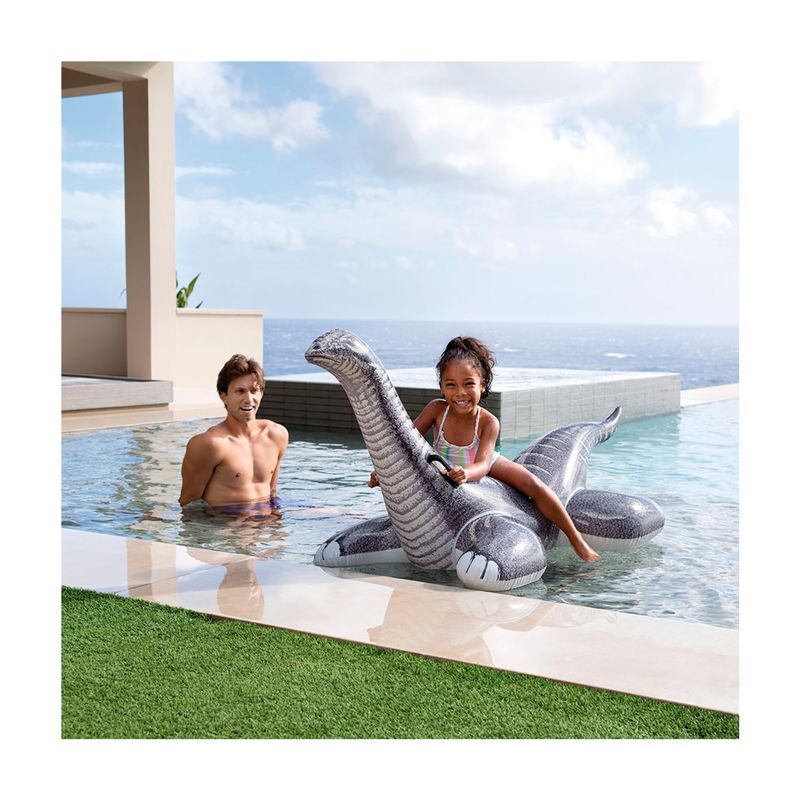 Flotador brontosaurio 1.78 x 0.94 m Intex, niña sentada sobre el inflable gris en una piscina con un hombre al fondo