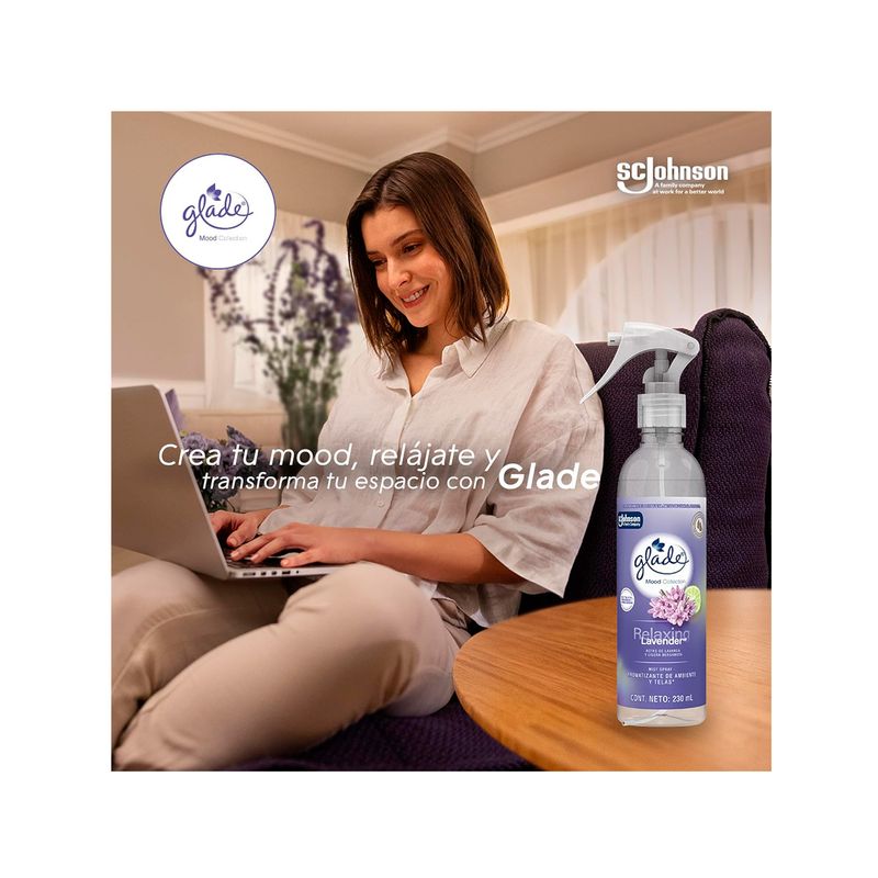 Aromatizante de ambiente y telas relaxing lavender 230 ml Glade, botella con atomizador junto a mujer usando laptop