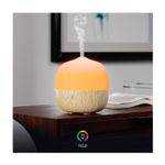 Difusor Mini Smart Nexxt, encendido con luz naranja y vapor saliendo, sobre una mesa de madera junto a un libro