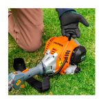 Desbrozadora gas 30 cc 17 pulgadas curva Truper, detalle del motor naranja sobre el césped con mano accionando el arranque